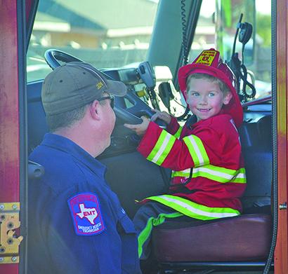 John Ellis Jamison, 4, sat behind the wheel of a Snyder Fire Department fire truck while firefighter Nathan Hines watches on at National Night Out at the Villages at Snyder on Tuesday. 