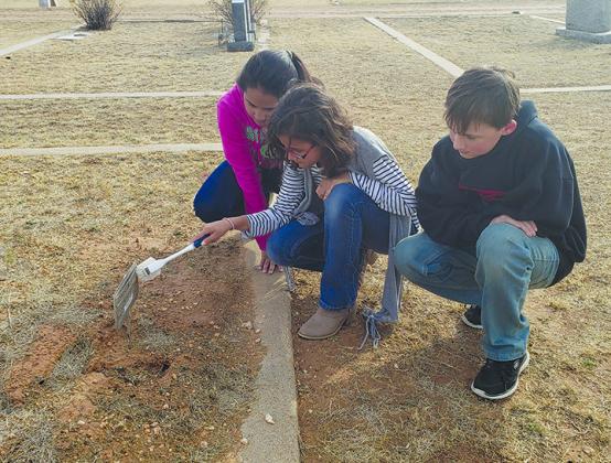 Snyder Junior High School students (l-r) Makayla Deleon, Mela Ramos and Michael Cheyne brush dirt off a grave marker at Snyder Cemetery. Students of the Afterschool Centers for Education program were planting flags on veterans’ graves and sprucing up the cemetery Friday in recognition of Veterans Day.