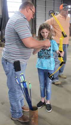 Justin Derryberry helped his daughter, Ashlyn Derryberry, with her bow during 4-H archery practice. In the background is coach Mike Hale observing the class.