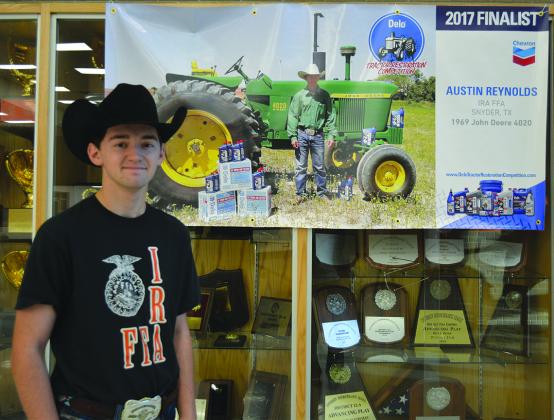 Austin Reynolds stands next to his national finalist poster in the foyer of the Ira ISD school.