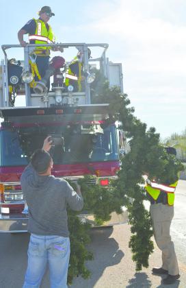 Snyder firefighters Nathan Evans and Ben Poe (in truck) take part of the garland swag from Deputy Fire Marshal Nathan Hines that is now hanging over College Ave. The firefighters hung the swag for the Snyder Chamber of Commerce, which purchased the new holiday decorations. Taking pictures of the hanging is the chamber’s events coordinator, Josh Ortegon.