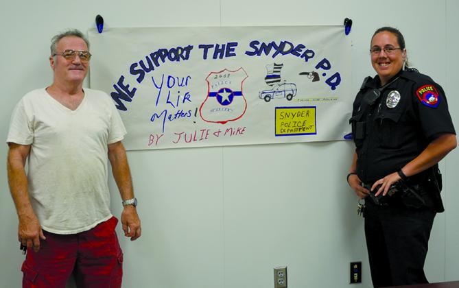 Micheal Holloway (left) and Snyder police officer Whitney Merket are shown with a banner Holloway and his wife, Julie, made to mark Police Appreciation Week. Julie Holloway also baked brownies for the local officers.