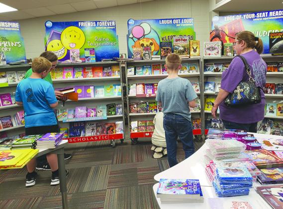 (l-r) fourth-grader Carson Graf and his mother, Melanie Graf, fifth-grader Tynan Petty, Anthony McCauley and mother, Denise McCauley look over the books offered at the Scholastic Book Fair Monday evening at Snyder Intermediate School’s Family Night.