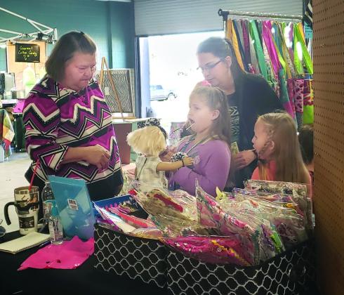 Cathy Hale, left, of Brownwood tells customers Leighton Ball, 8, Nancy Ball and Kinsley Ball, 6, about the American Girl doll clothes she was selling Friday at the March Madness Market Days at the Towle Park Armory. About 26 vendors  from Texas and Oklahoma displayed wares at the market Friday and Saturday.