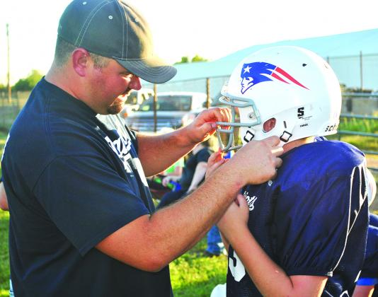 Coach Mike Wilson helped Brenson Halfor strap on his helmet during a Snyder Youth Football League 11- and 12-year-old football game between the Patriots and Cowboys at the Scurry County Boys & Girls Club Monday night.